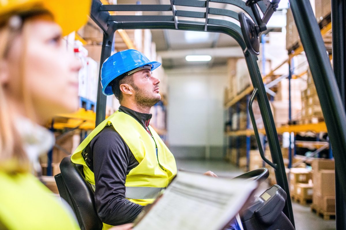 Young workers working together. Man forklift driver and a woman in a warehouse.