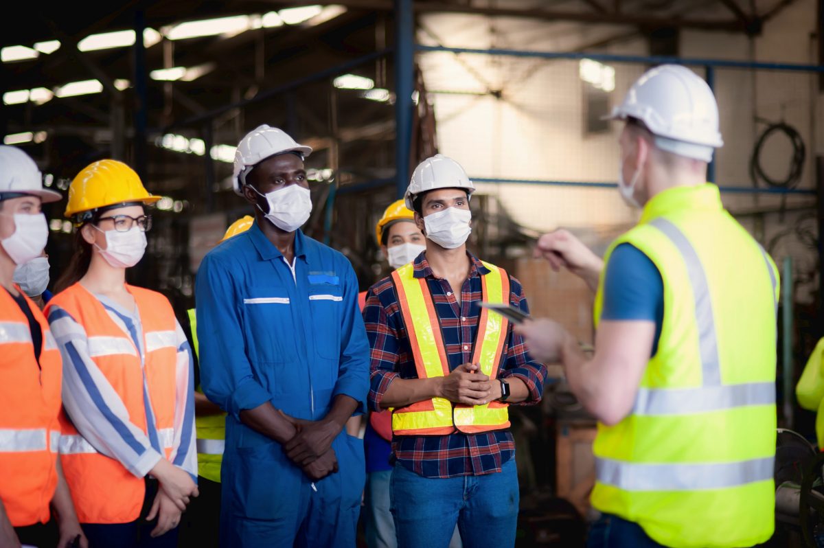 A Team Of Technicians, Foreman And Engineers Accepting Assignments From A Manager Or Supervisor In The Morning Meeting Before Work In Which Everyone Wear Surgical Masks To Prevent The Coronavirus