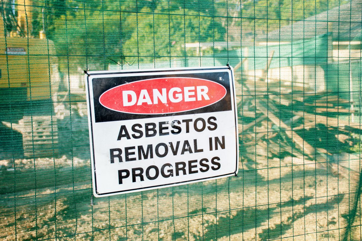 Una señal de advertencia de peligro de amianto en una valla de la obra donde se está demoliendo una casa antigua
