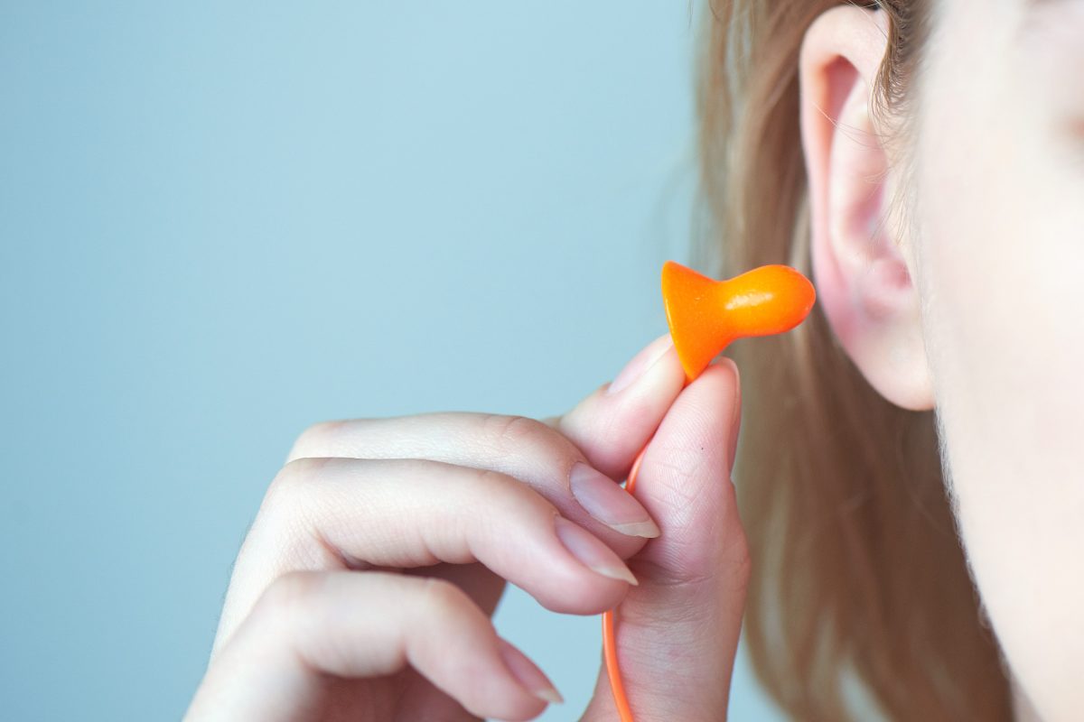 Chica rubia se pone tapones en la oreja de cerca sobre fondo blanco